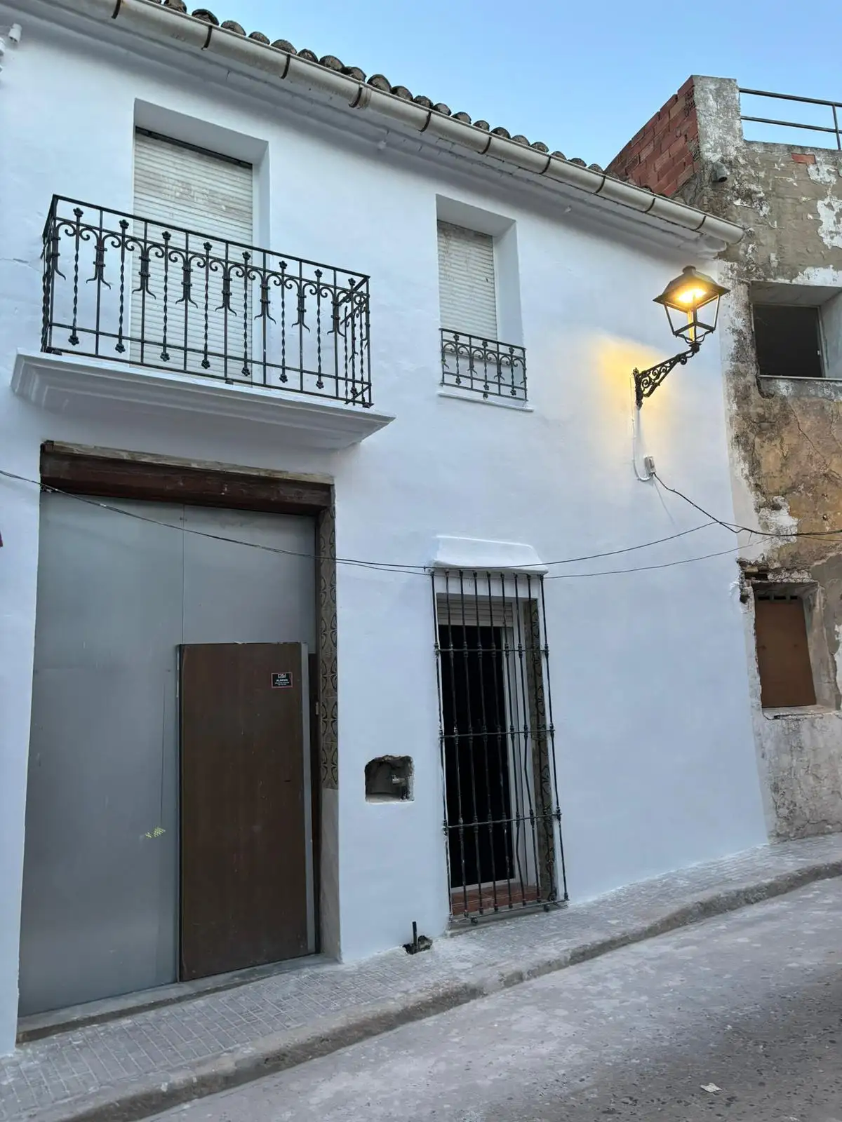 Rehabilitación de fachada blanca con balcones de forja negra y farola clásica en Valencia
